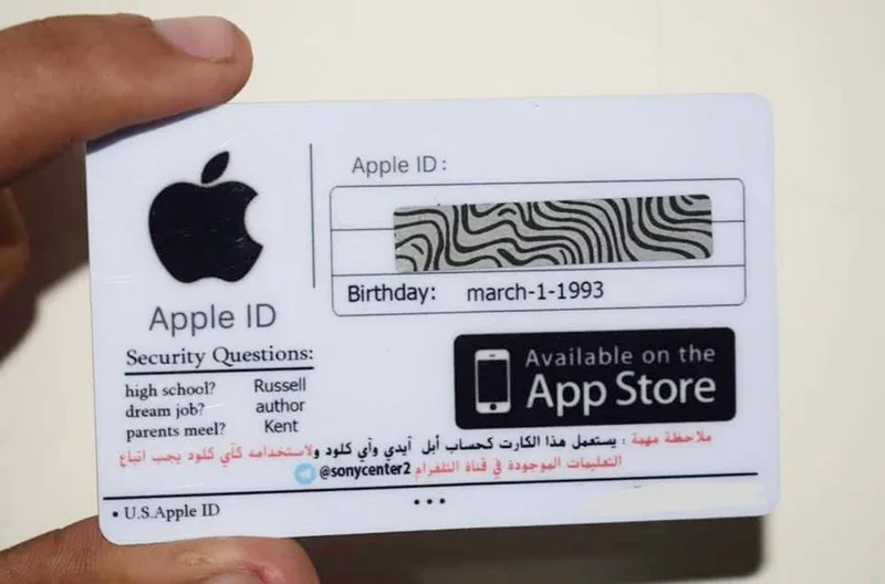 يد تحمل بطاقة بيضاء عنوانها Apple ID، بريد الحساب فيها مخفيّ تحت طبقة تُزال بالحكّ، وعليها تاريخ ميلاد وثلاثة أسئلة أمان مع إجاباتها، وشارة App Store، ومعرّف قناة على تلغرام، وعبارة U.S. Apple ID.
